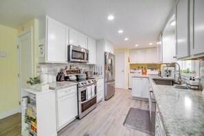 A modern kitchen with white cabinets, stainless steel appliances, and a marble countertop.