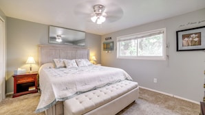 A bedroom with a large bed, a nightstand, a ceiling fan, a window, and a wall-mounted mirror.