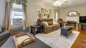 A living room with a brown leather sofa, a grey armchair, a wooden coffee table, and a fireplace with a TV. - 3 Mi to Dtwn Springfield: Winter Retreat w/ Office (Springfield)
