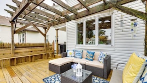 A covered patio with a wooden deck, a wicker sofa with cushions, and a glass coffee table.