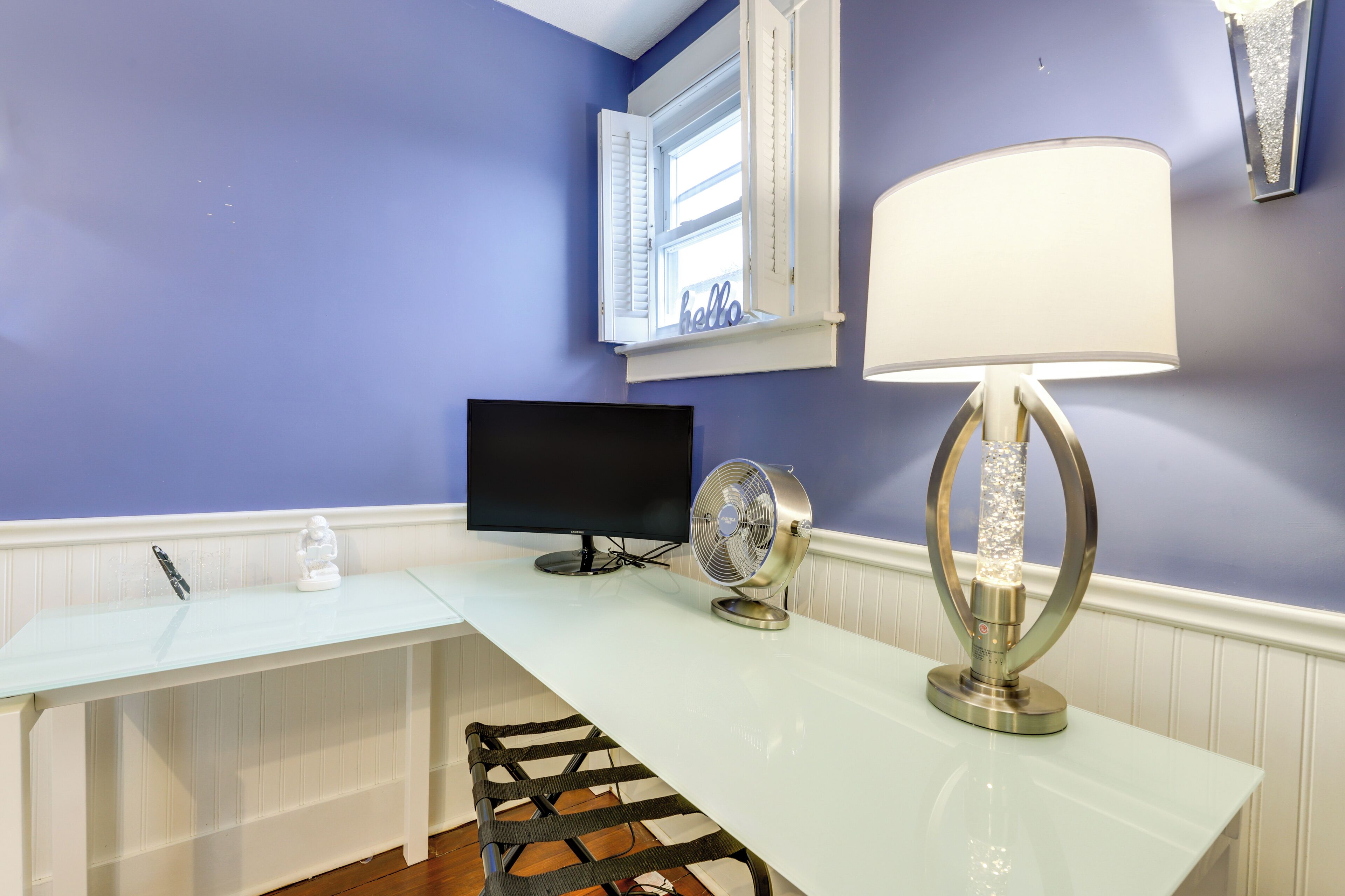 Una habitación con un escritorio blanco, un televisor de pantalla plana, un ventilador y una lámpara decorativa.