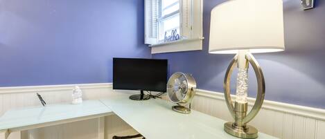 Una habitación con un escritorio blanco, un televisor de pantalla plana, un ventilador y una lámpara decorativa.