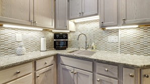 A kitchen with light wood cabinets, a granite countertop, a built-in oven, and a tiled backsplash.