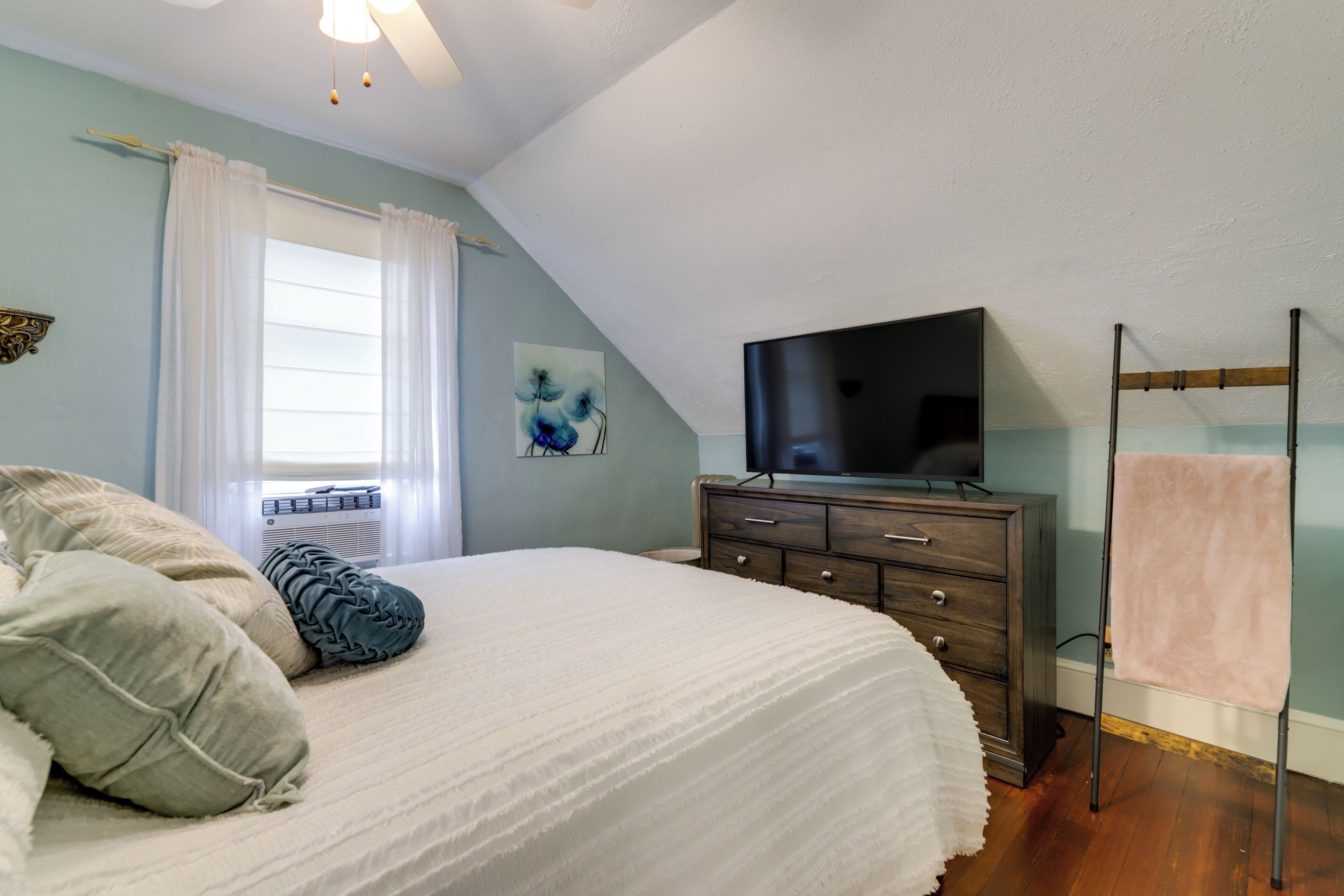 Un dormitorio con cama, cómoda, televisor y ventana con cortinas.