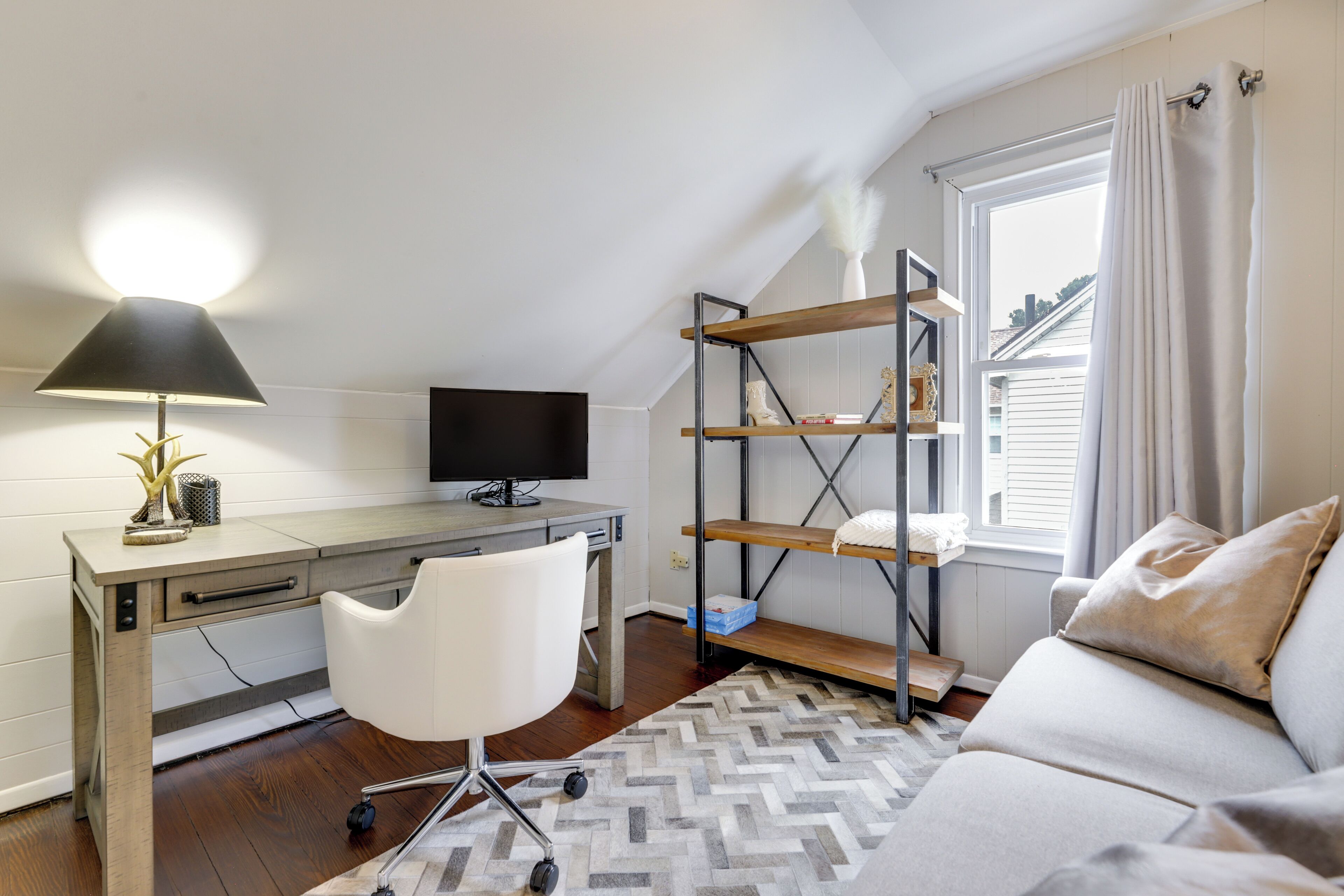 A bedroom with a desk, a chair, a TV, a bed, a window, and a shelving unit.