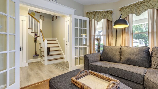 A living room with a gray sofa, a patterned ottoman, and a staircase leading to another room.