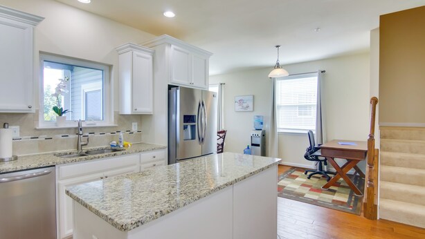 A modern kitchen with white cabinetry, granite countertops, a stainless steel refrigerator, and a dining area with a wooden table and chairs.