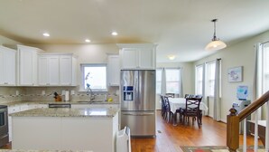 A kitchen with white cabinets, a stainless steel refrigerator, granite countertops, and a dining area with a table and chairs.