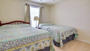A bedroom with two beds, a ceiling fan, a window with curtains, and a bedside lamp.