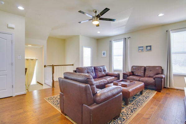 A spacious living room with a brown leather sectional sofa, a ceiling fan, and a large window with blinds. - Bay Views! Luxury Family Retreat in Ocean City (Ocean City)