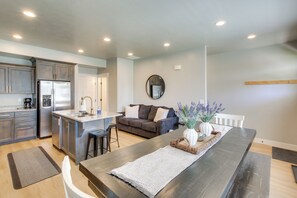 A modern kitchen with a central island, built-in appliances, and a dining area with a large table. - Garden City Townhome, Close to Parks + Downtown! (Garden City)