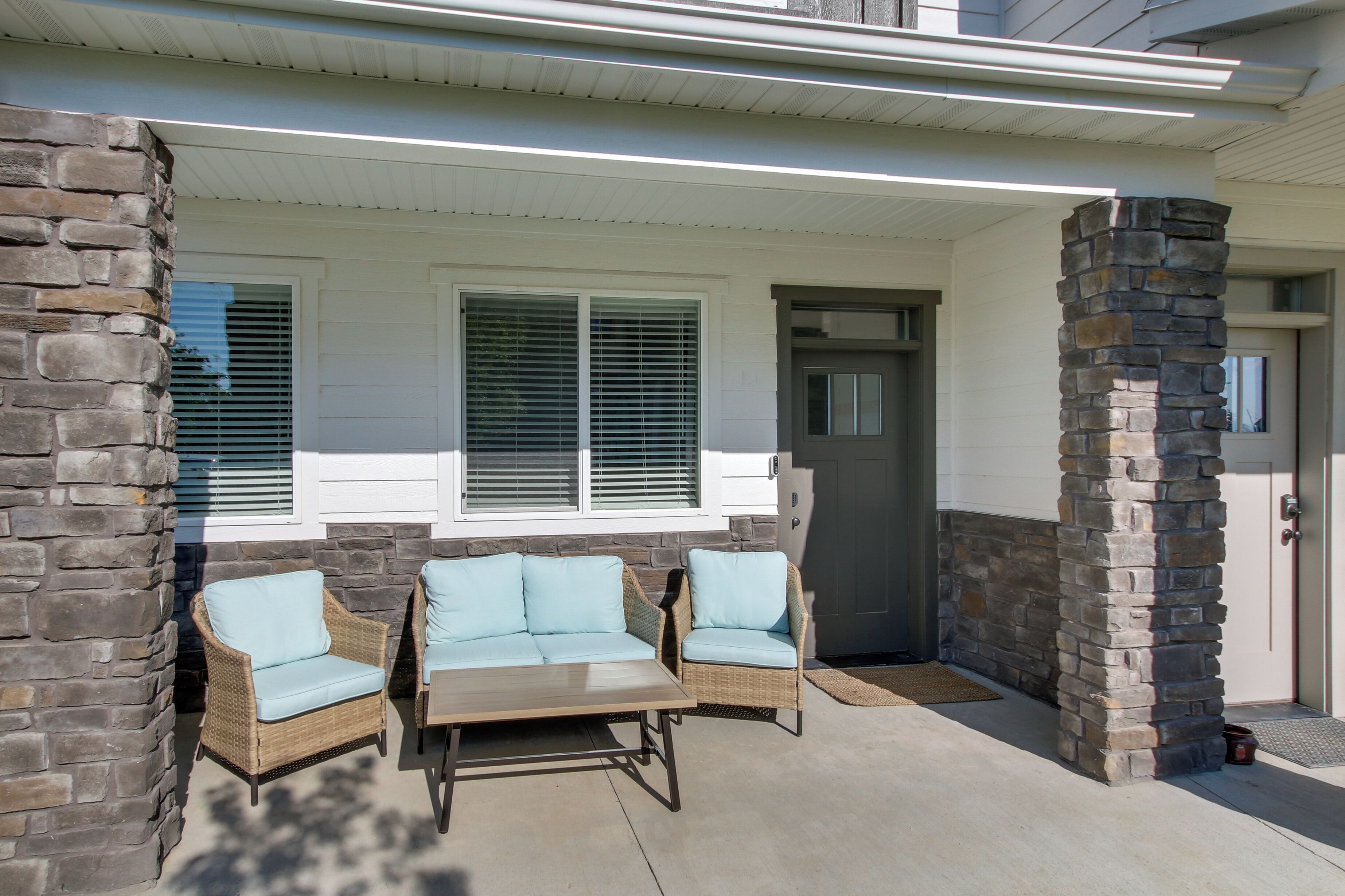 A covered patio with wicker furniture and stone pillars.