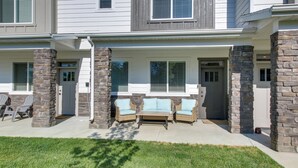 A two-story townhouse with stone pillars, a front porch with wicker furniture, and a small lawn. - Garden City Townhome, Close to Parks + Downtown! (Garden City)