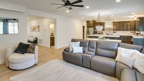 Ein modernes Wohnzimmer mit einem grauen Ecksofa, einem weißen Sessel und einem Deckenventilator.