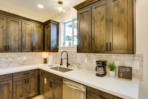 A kitchen with wooden cabinets, a white countertop, a sink, a coffee maker, and a sign about the wifi password. - Garden City Vacation Rental: Walk to Bear Lake (Garden City)