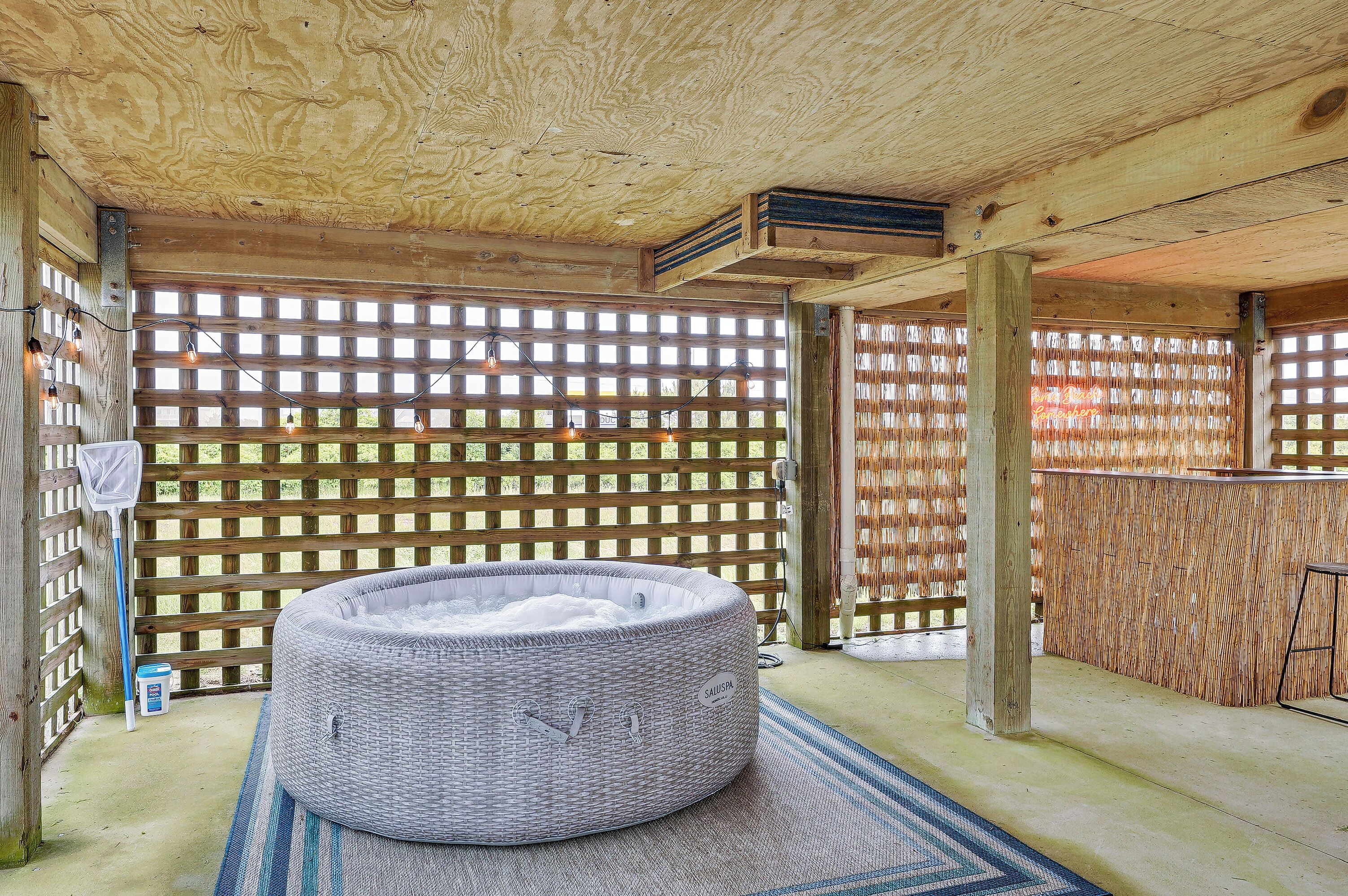 Una terraza de madera con un jacuzzi, una valla de bambú y una zona de bar.