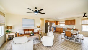 A spacious living room with a sofa, chairs, and a dining table. A kitchen with wooden cabinets and appliances is visible in the background. - Nags Head Vacation Rental w/ Hot Tub: Near Beach! (Nags Head)