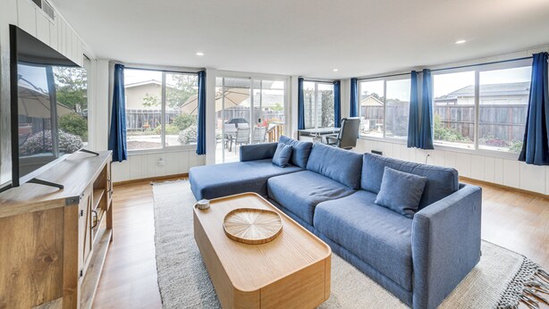 A modern living room with a sectional sofa, wooden coffee table, and large windows with curtains. - Seaside Vacation Rental w/ Patio Near Monterey Bay (Seaside)