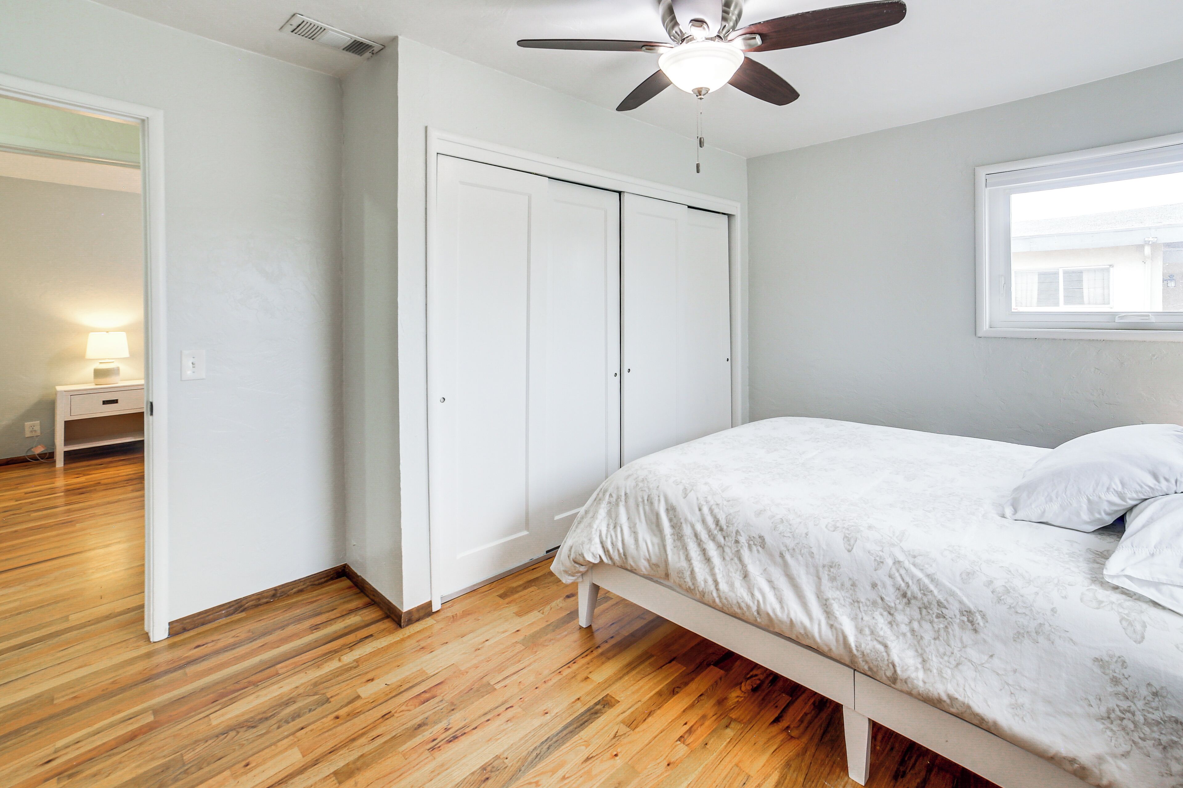 A bedroom with a bed, wooden flooring, a ceiling fan, and a window.