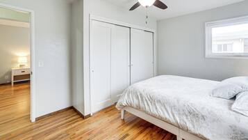 A bedroom with a bed, wooden flooring, a ceiling fan, and a window.