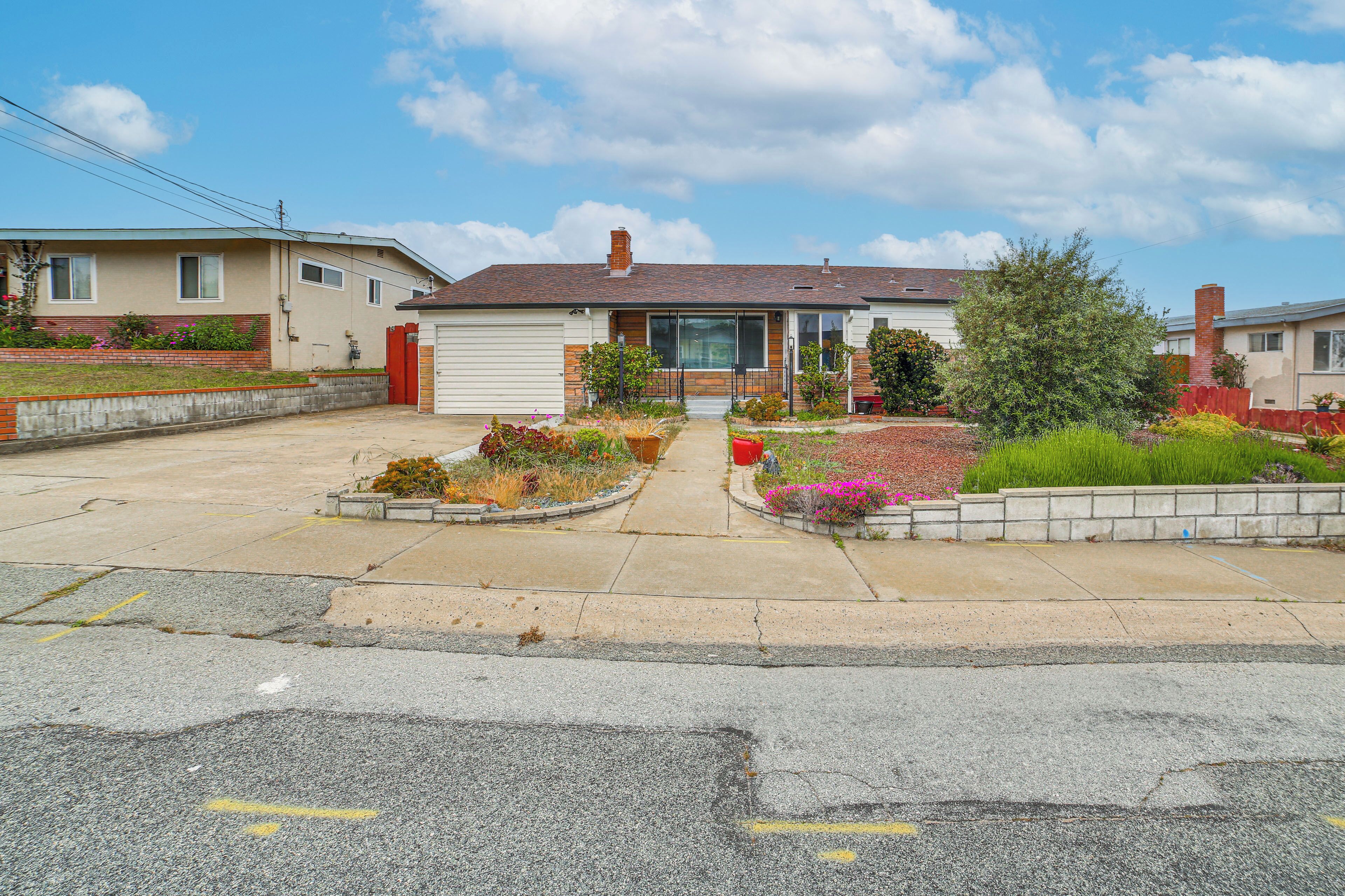 A single-story house with a garage, a front yard with various plants, and a clear sky.