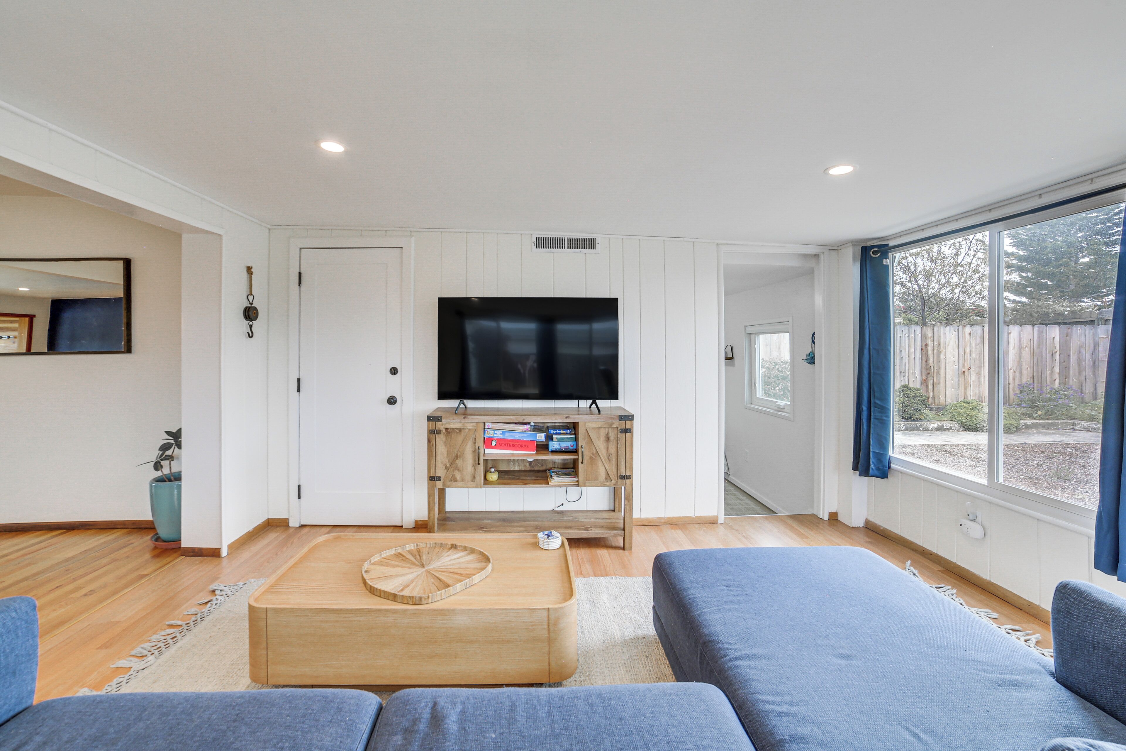 A modern living room with a large flat-screen TV, wooden coffee table, and blue sofas.