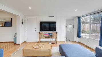 A modern living room with a large flat-screen TV, wooden coffee table, and blue sofas.