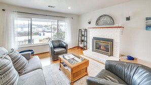 A living room with a fireplace, leather sofas, a coffee table, and a view through large windows. - Seaside Vacation Rental w/ Patio Near Monterey Bay (Seaside)