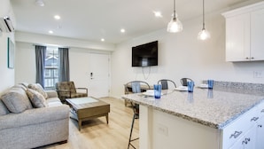 A modern kitchen with a granite countertop, a dining area with a wooden table and chairs, and a living room with a sofa and a television. - Community Pool Access: Rehoboth Beach Unit! (Rehoboth Beach)