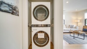 A laundry room with two stacked washers and dryers, a white couch, and a coffee table in a modern living area. - Beautiful Cape May Cottage: Walk to Beach & Mall! (Cape May)