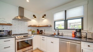 A modern kitchen with white cabinets, stainless steel appliances, and a window with blinds. - Beautiful Cape May Cottage: Walk to Beach & Mall! (Cape May)