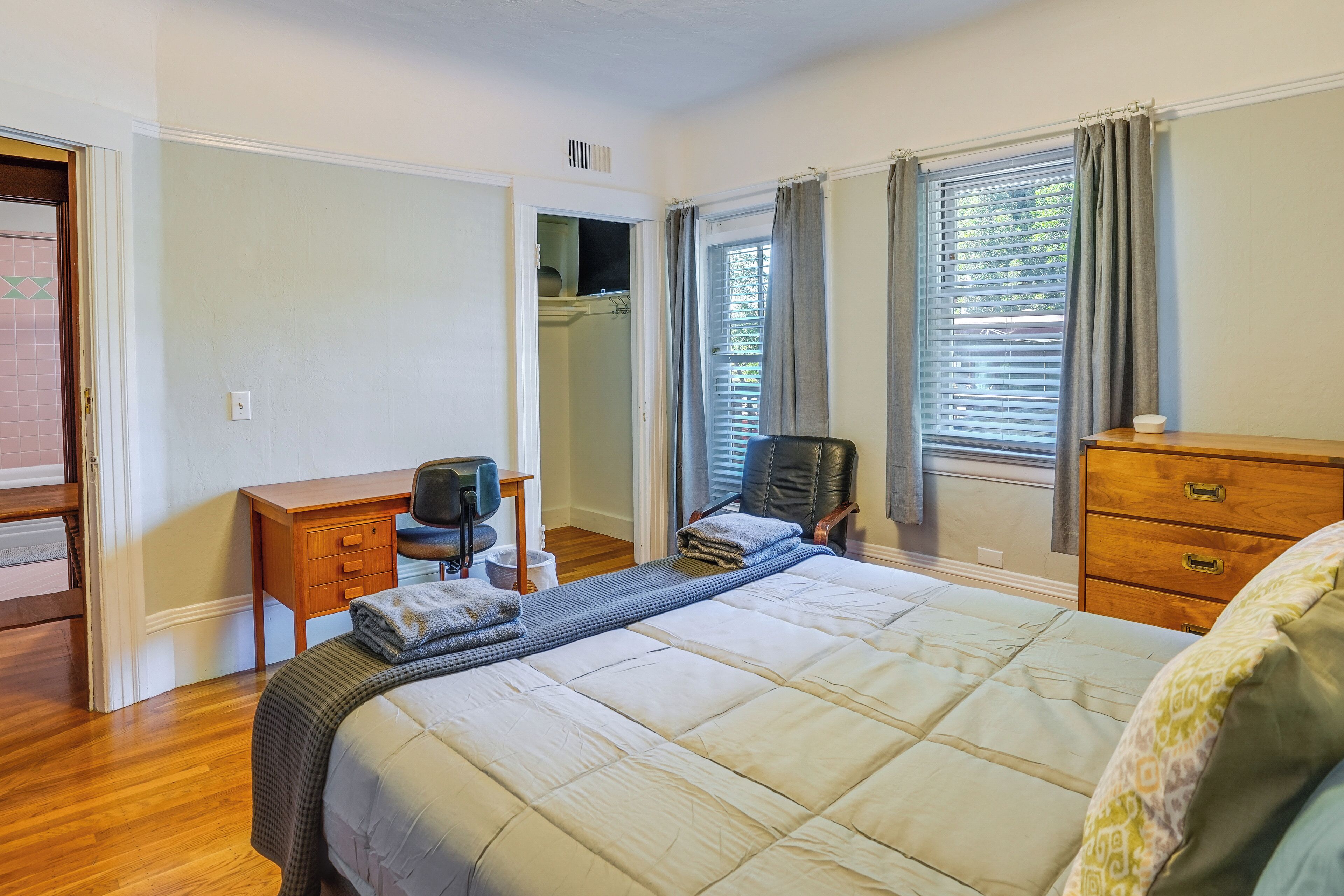 A bedroom with a large bed, a desk, a chair, a dresser, and a closet.