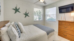 A bedroom with a bed, two starfish wall decorations, a ceiling fan, a TV, and a wooden dresser.