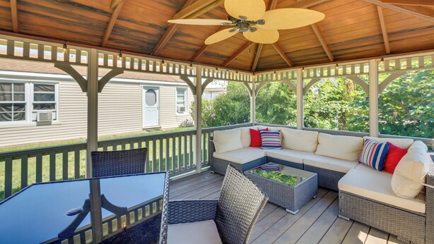 A covered outdoor patio with a ceiling fan, wicker furniture, and a view of a house in the background.