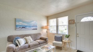 A living room with a beige sofa, a glass coffee table, a striped armchair, a lamp, and a painting of a beach scene.