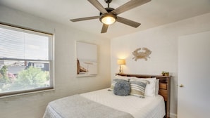 A bedroom with a bed, a ceiling fan, a window with blinds, a bedside table with a lamp, and a door. - Wildwood Crest Getaway w/ Deck, Walk to Beach! (Wildwood Crest)