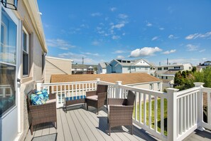 A deck with wicker furniture and a white railing, overlooking a residential area with houses.