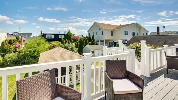 A deck with wicker furniture and a white railing, overlooking a residential neighborhood with houses and greenery. - Wildwood Crest Getaway w/ Deck, Walk to Beach! (Wildwood Crest)