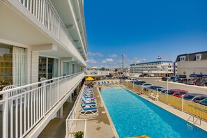 A pool area with lounge chairs, a clear blue sky, and a view of the street and buildings in the background. - Beachfront Wildwood Vacation Rental w/ Pools! (Wildwood Crest)