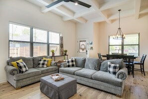 A spacious living room with a grey sectional sofa, a coffee table, and a dining area with a table and chairs.