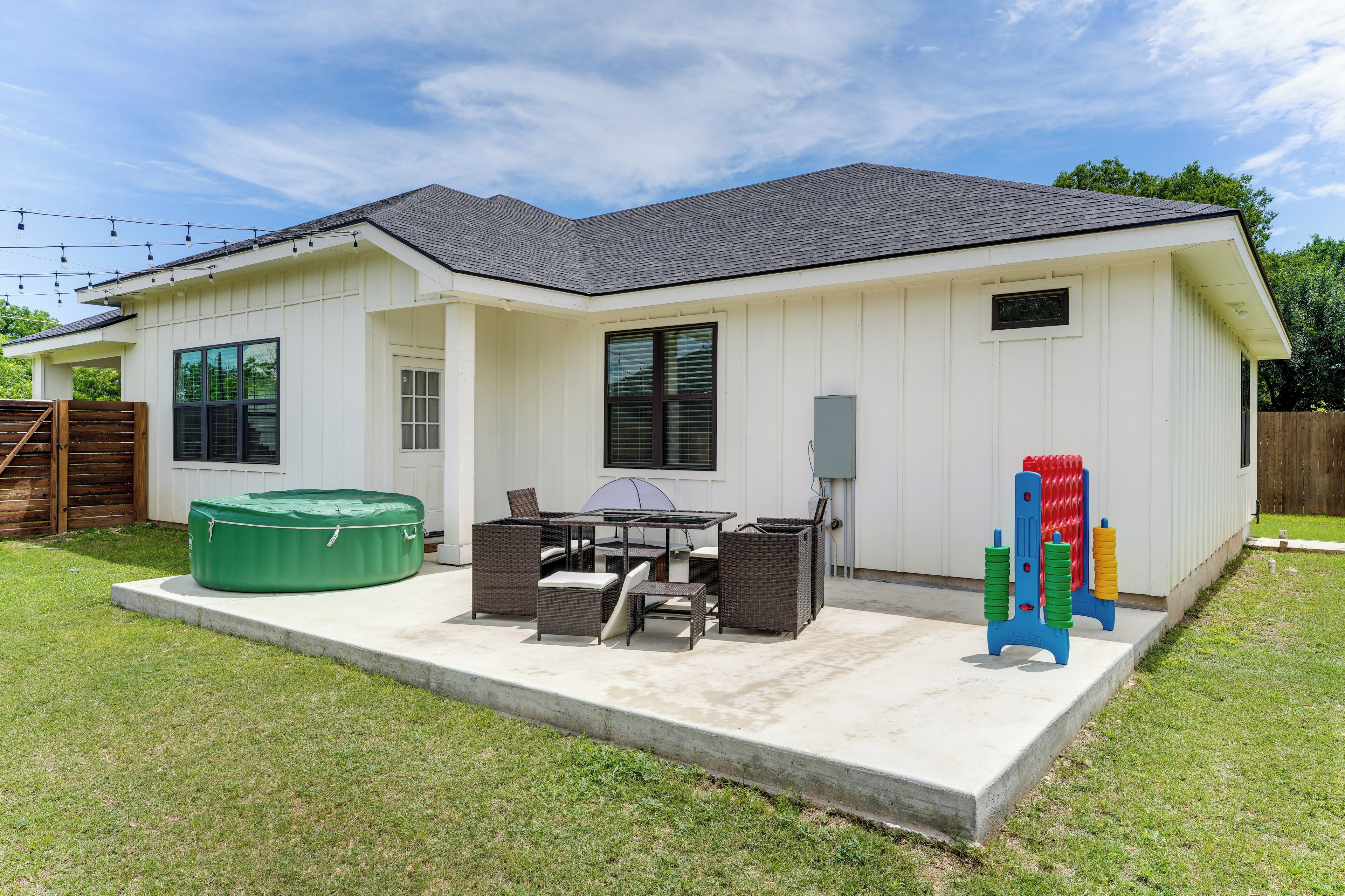 Een wit huis met een overdekte patio, een jacuzzi en tuinmeubilair.