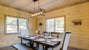 Une salle à manger en bois avec une grande table dressée pour six personnes, entourée de chaises rembourrées.