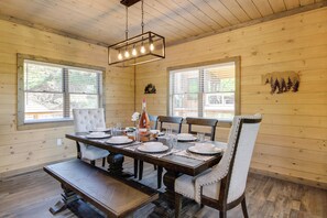 Une salle à manger en bois avec une grande table dressée pour six personnes, entourée de chaises rembourrées.