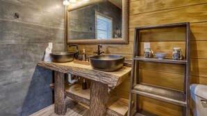 Une salle de bain avec un meuble-lavabo en bois, deux vasques, un grand miroir et une étagère contenant des articles de toilette.