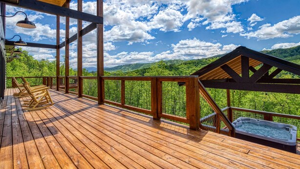A wooden deck with a hot tub, wooden railings, and a view of a forested mountain range. - Luxury Sevierville Cabin w/ Private Hot Tub! (Sevierville)