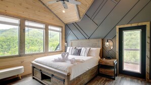 A bedroom with a wooden bed, a bench, and a view of a forest through large windows. - Luxury Sevierville Cabin w/ Private Hot Tub! (Sevierville)