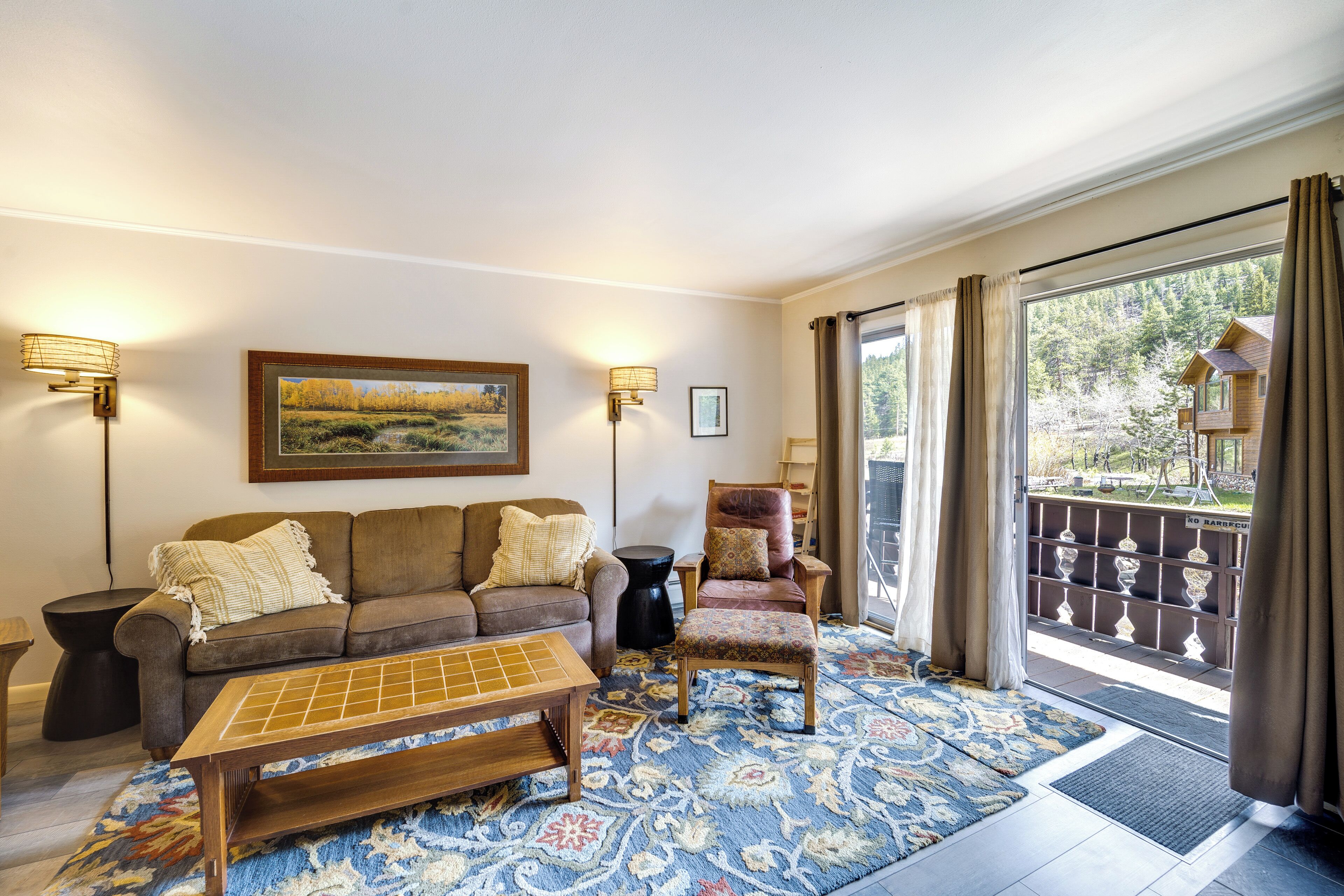 A living room with a sofa, armchair, and ottoman, a coffee table, a rug, and a painting on the wall.