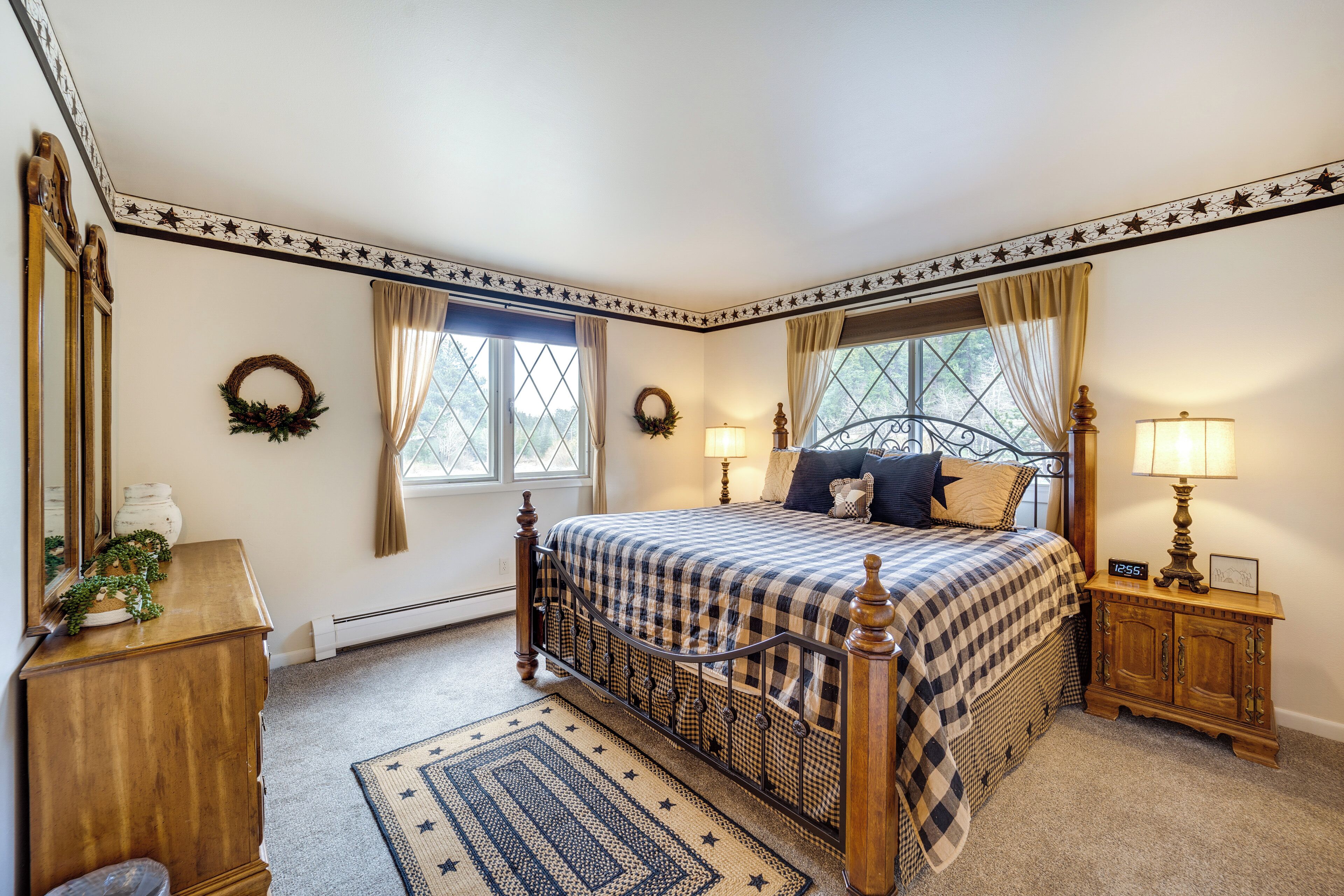 A bedroom with a checkered bedspread, two bedside lamps, a wooden nightstand, a dresser, and a star-patterned ceiling.