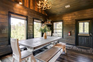 A wooden interior with a dining table, benches, and a chandelier.