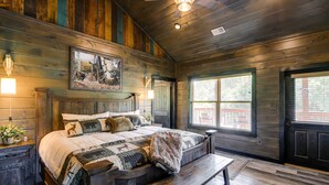 A rustic wooden bedroom with a large bed, a bench, and a painting on the wall.